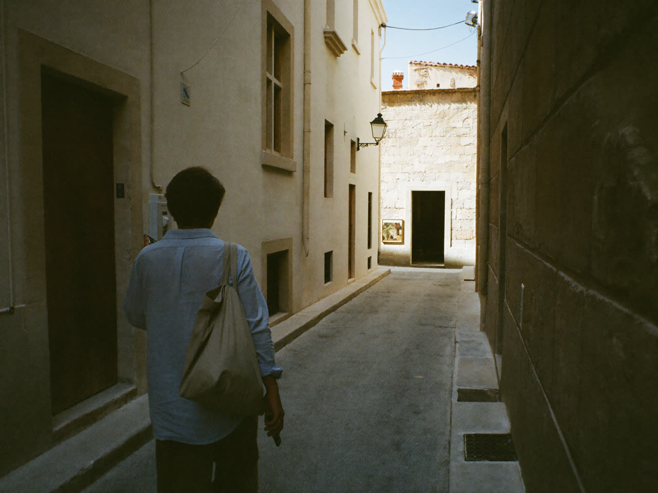 A traveller pausing in a limestone lane, phone in hand, looking toward a lit guesthouse doorway